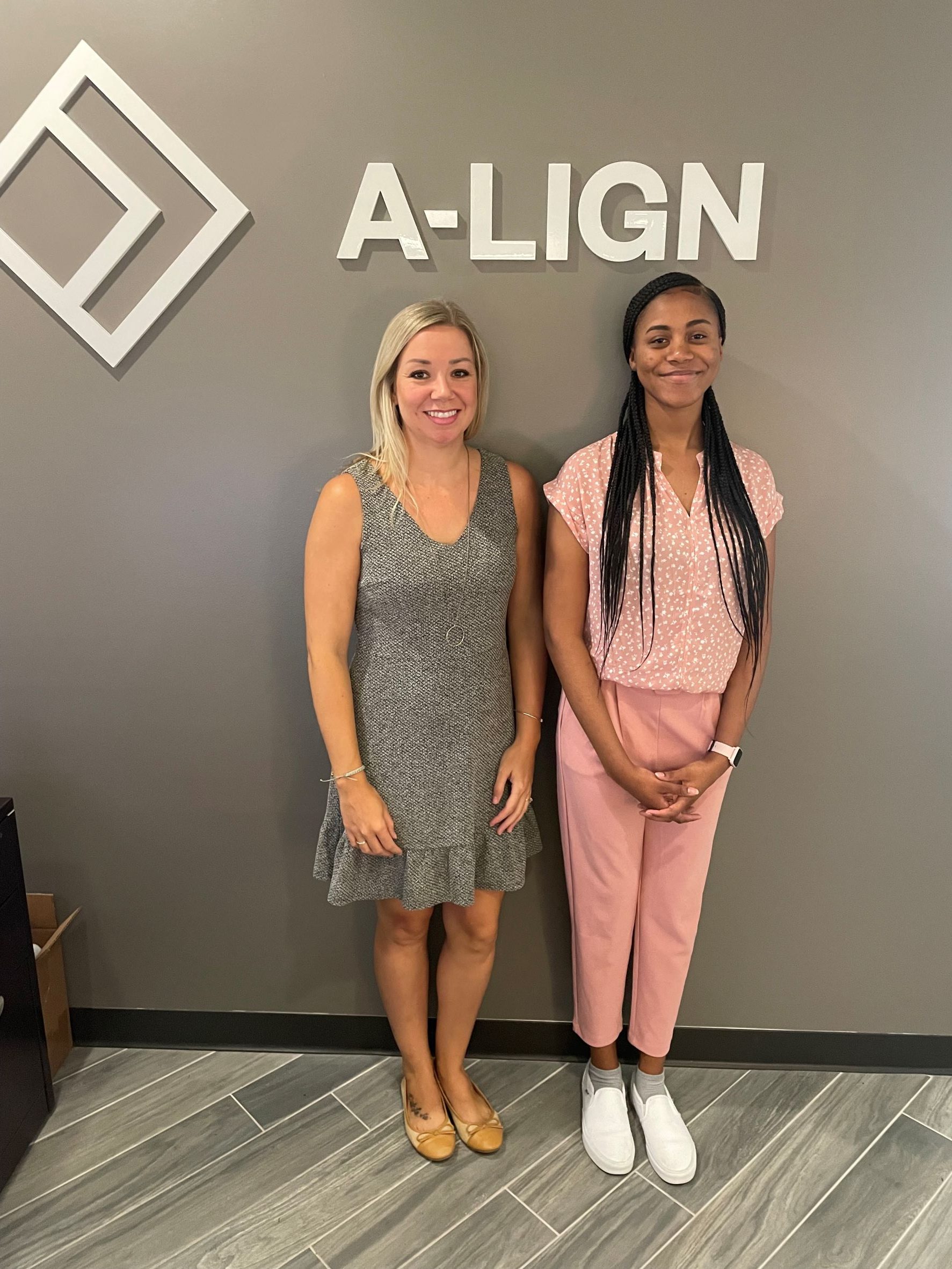 Female adult with her mentee standing in front of A-LIGN sign